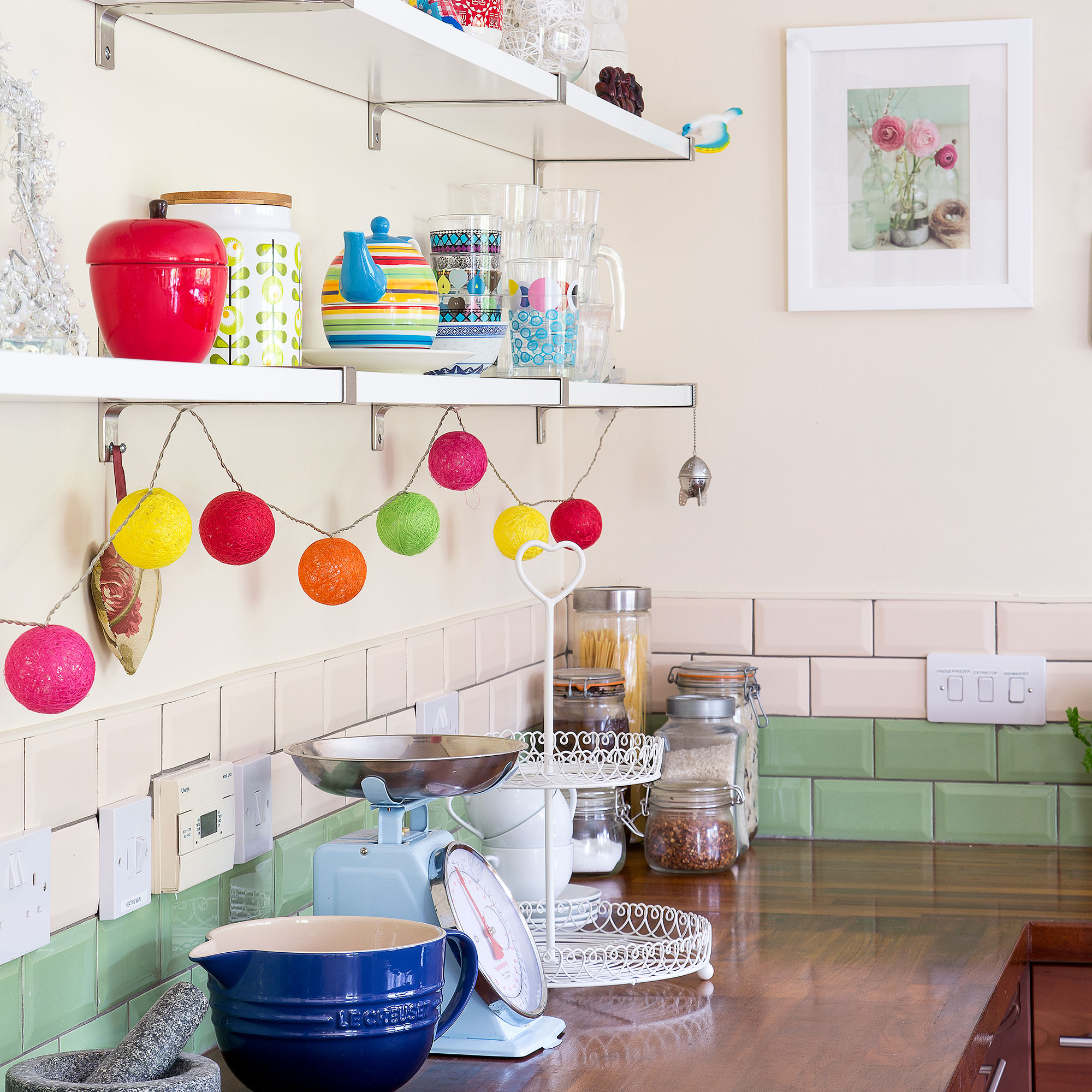 Dapur krem ​​dengan splashback ubin metro hijau dan merah muda dan rantai ringan berwarna