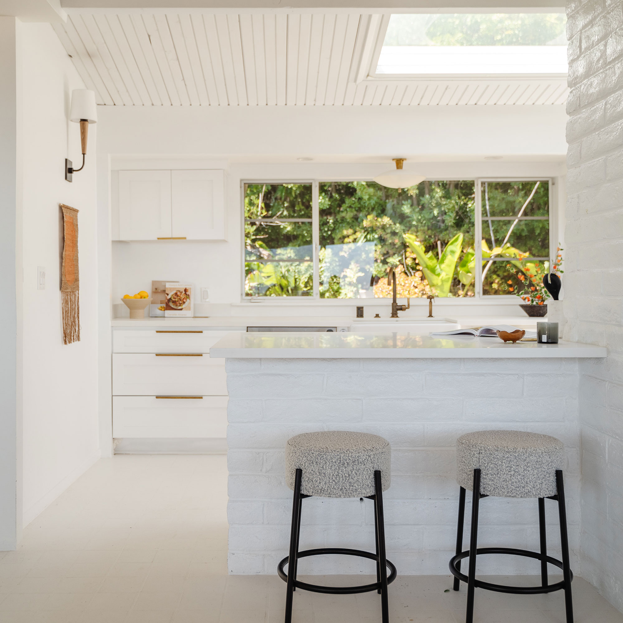 Dapur serba putih dengan kursi bar di konter dan jendela besar di belakang